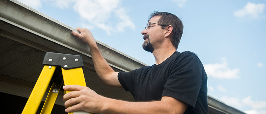 Man on ladder to inspect gutters