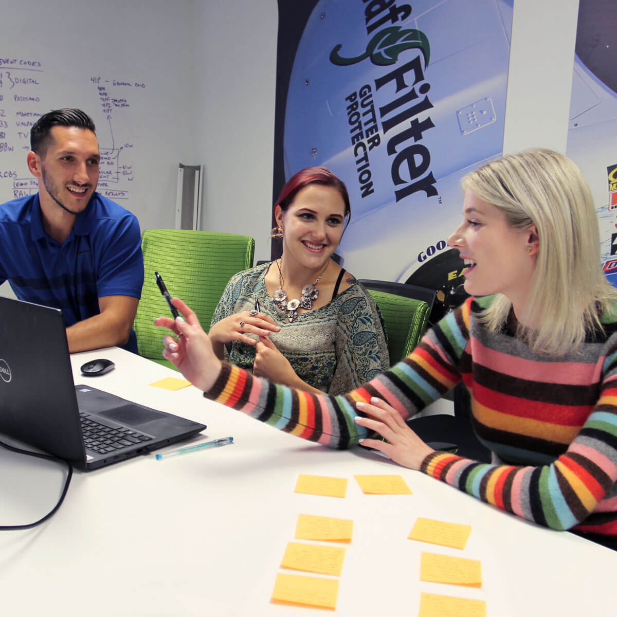 Three members of LeafFilter's social media team discuss strategy on a computer with a LeafFilter-branded NASCAR mural behind them