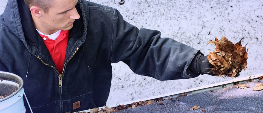 A gutter cleaner perches alongside a roof to clean gutters. Snow covers the grass in the background.