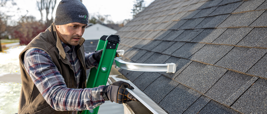 An installer, using a special ladder that leans against the roof rather than the gutters, fits LeafFilter on a home.